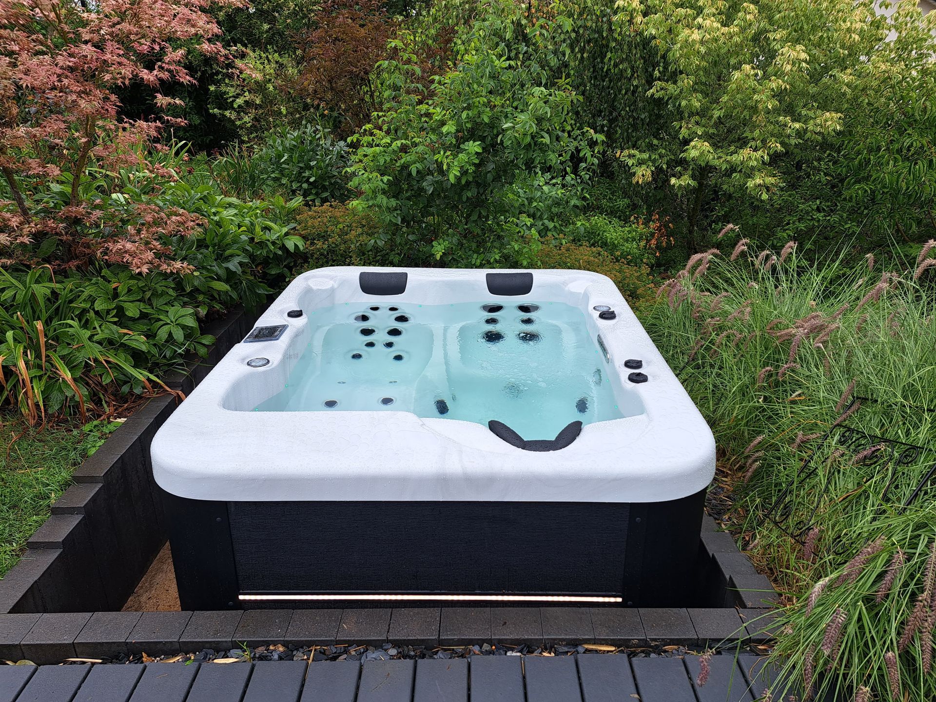 Un bain à remous est installé au milieu d'un jardin entouré d'arbres.