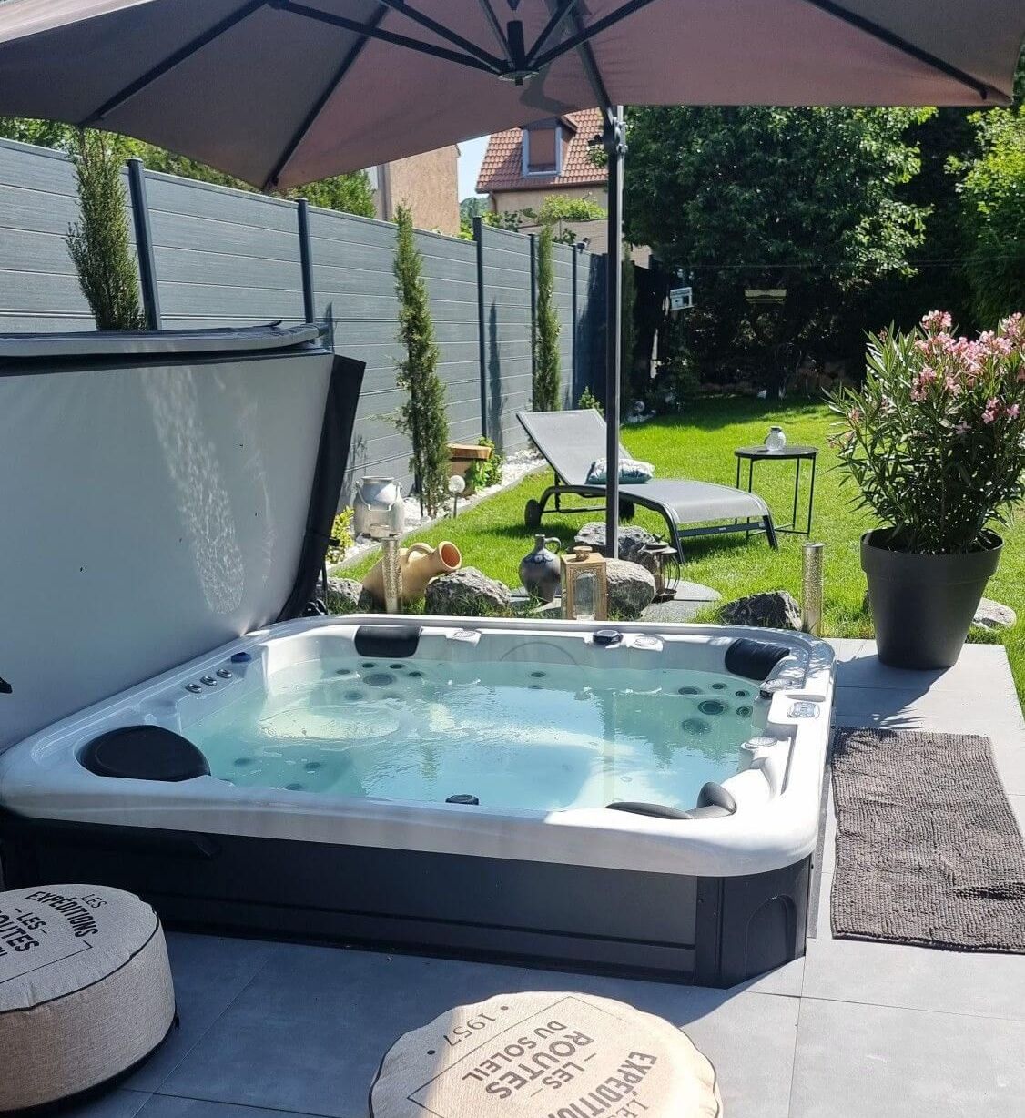 Un jacuzzi est installé sous un parasol dans un jardin