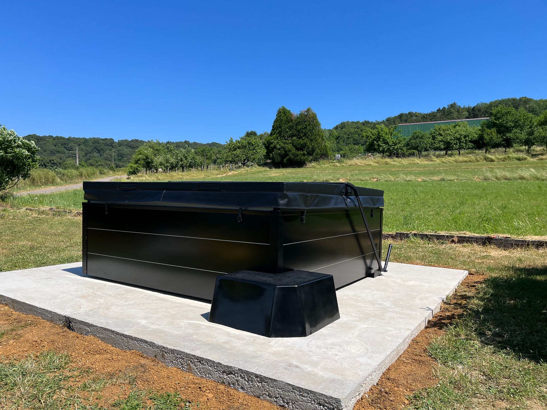 Un jacuzzi noir est posé sur une plate-forme en béton dans un champ.