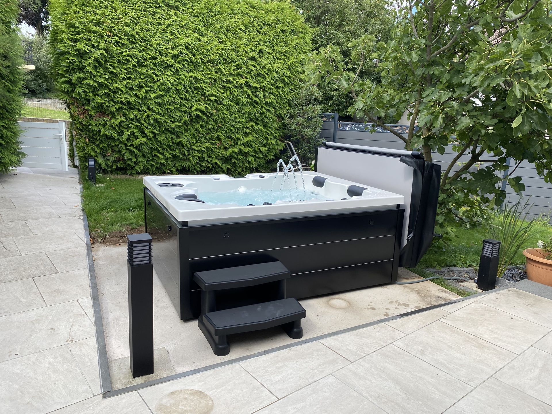 Un bain à remous est installé sur une terrasse à côté d'une haie.