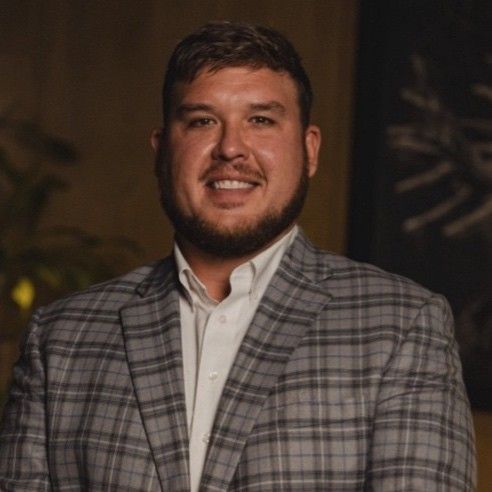 A man with a beard is wearing a plaid suit and smiling.