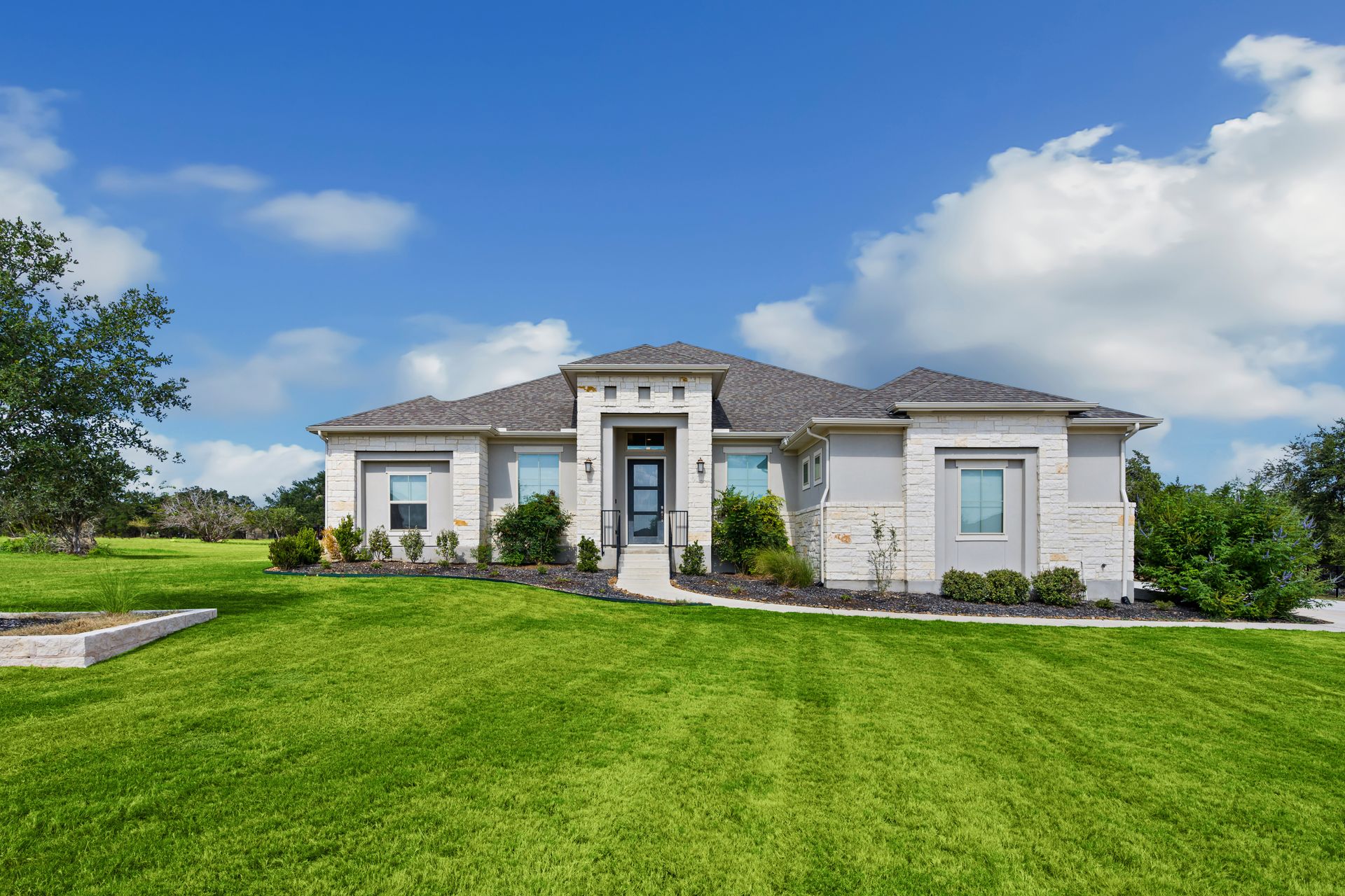 Single-story stone house with a large green lawn and blue sky