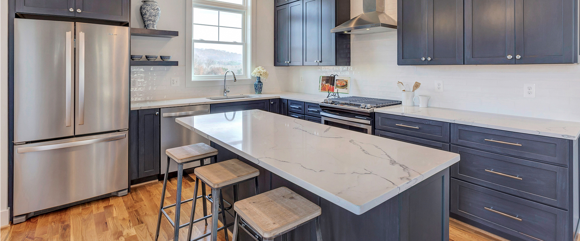 Modern kitchen with navy cabinets, white countertops, stainless steel appliances, and a kitchen island with stools.