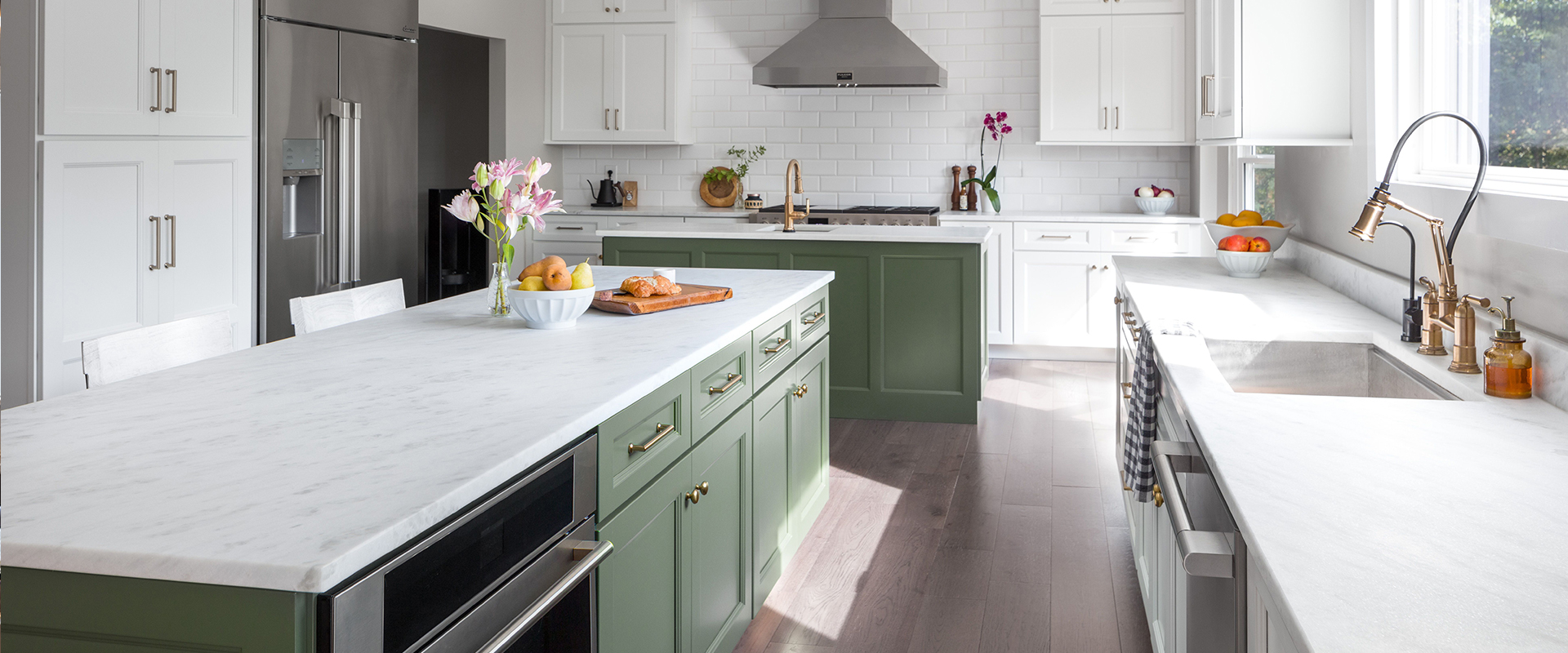 A modern kitchen with green island, white countertops, stainless steel appliances, and light wood floors.