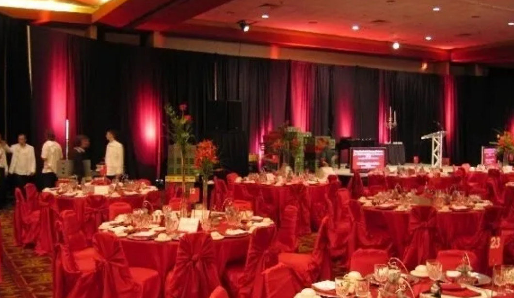 Red-themed banquet hall set for an event; red tables, chairs, and lighting against a black backdrop.