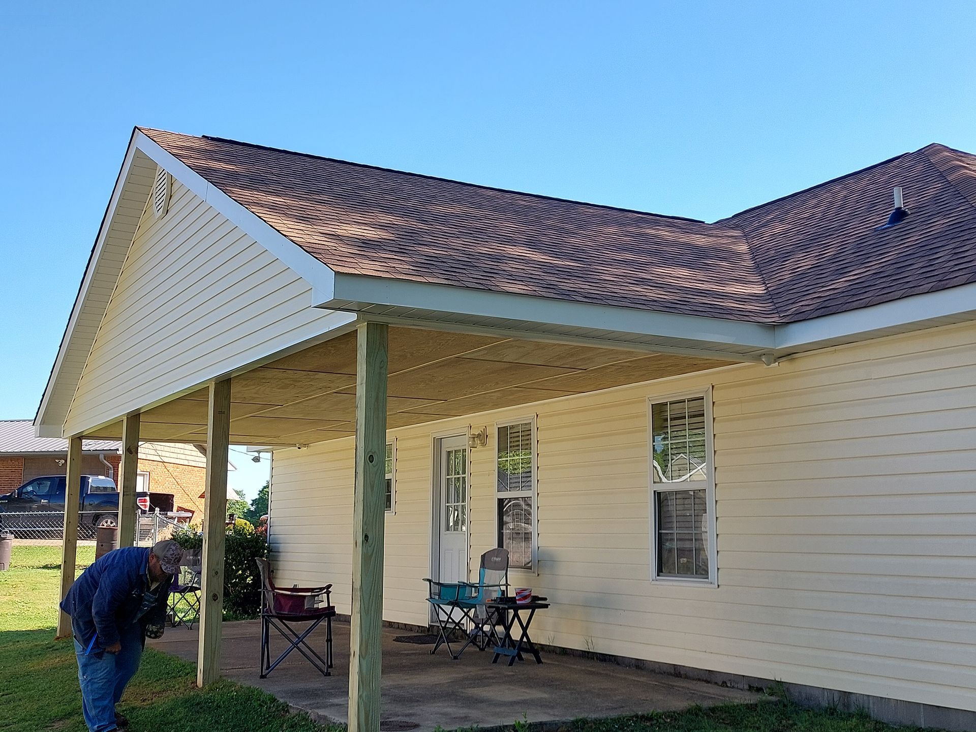 Single-story beige house with red roof, front porch, and a person bending near the lawn.