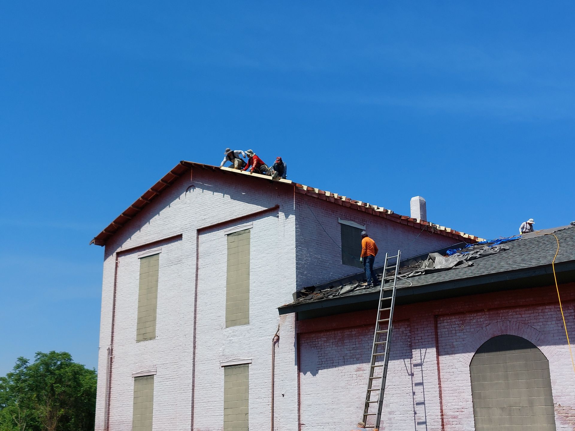 Workers on a roof repairing a white house with ladders under a clear blue sky