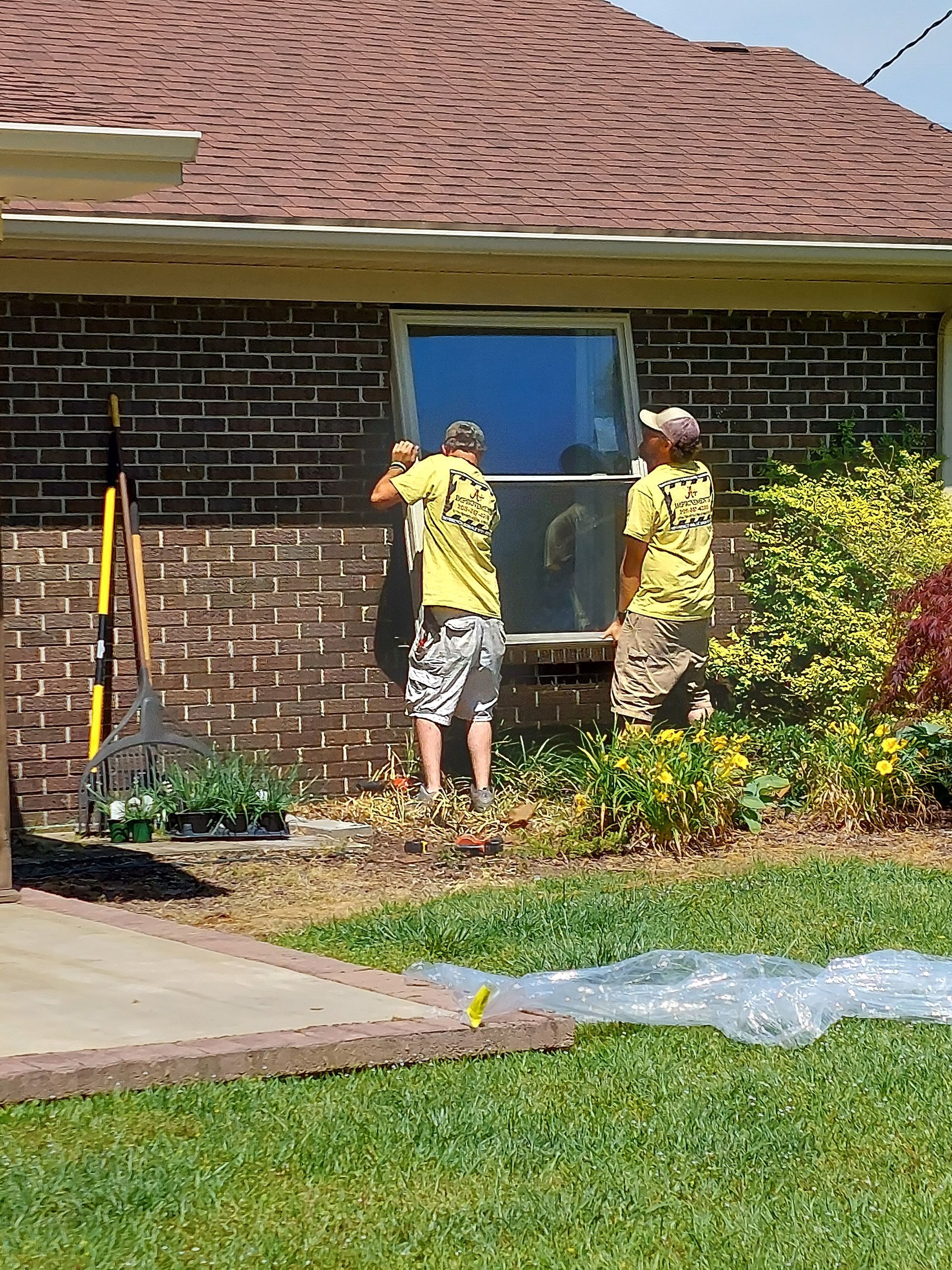 Two workers in yellow shirts measuring a brick house window during exterior repairs