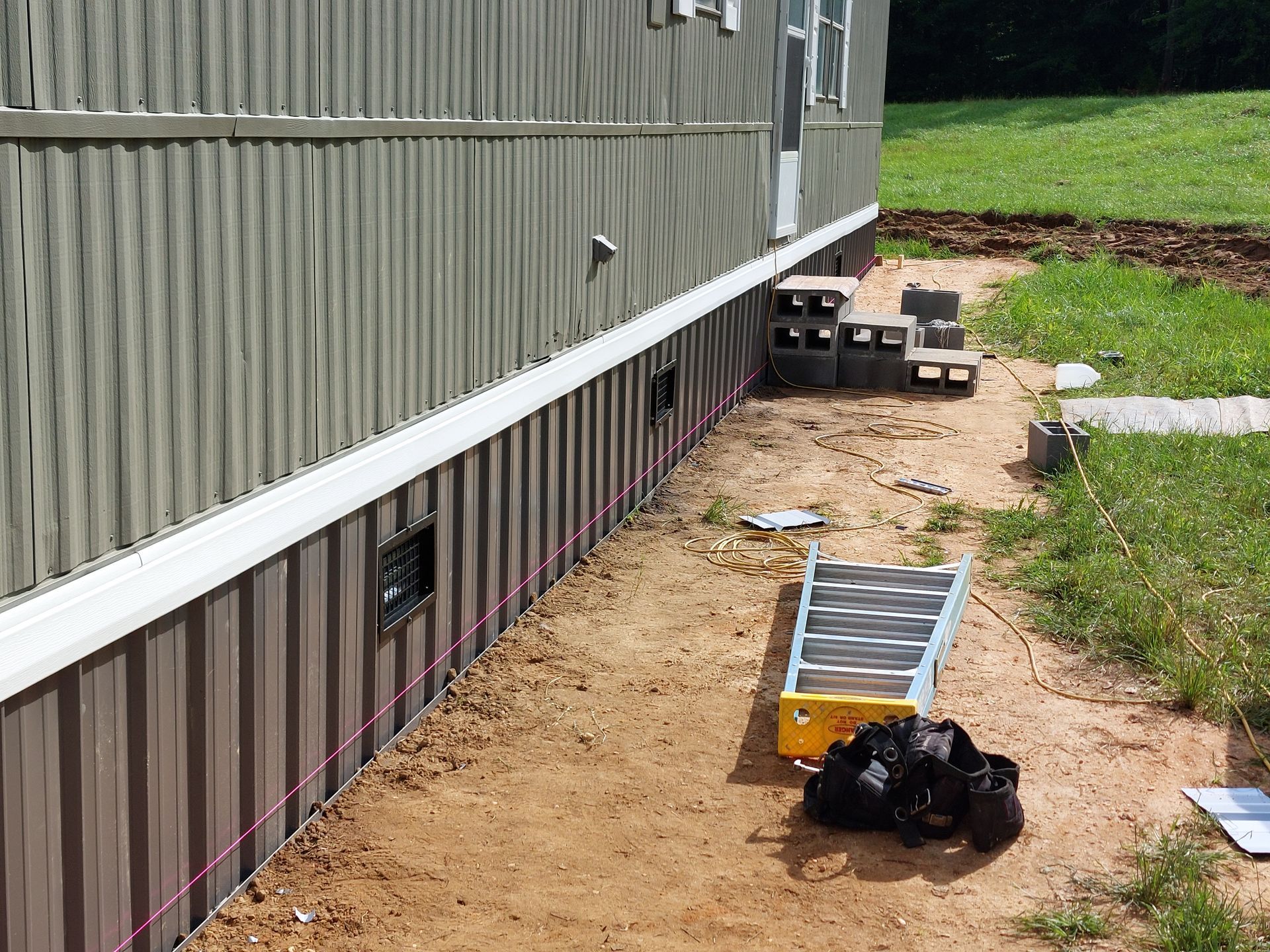 Siding repair materials along a house foundation beside a dirt path and grass