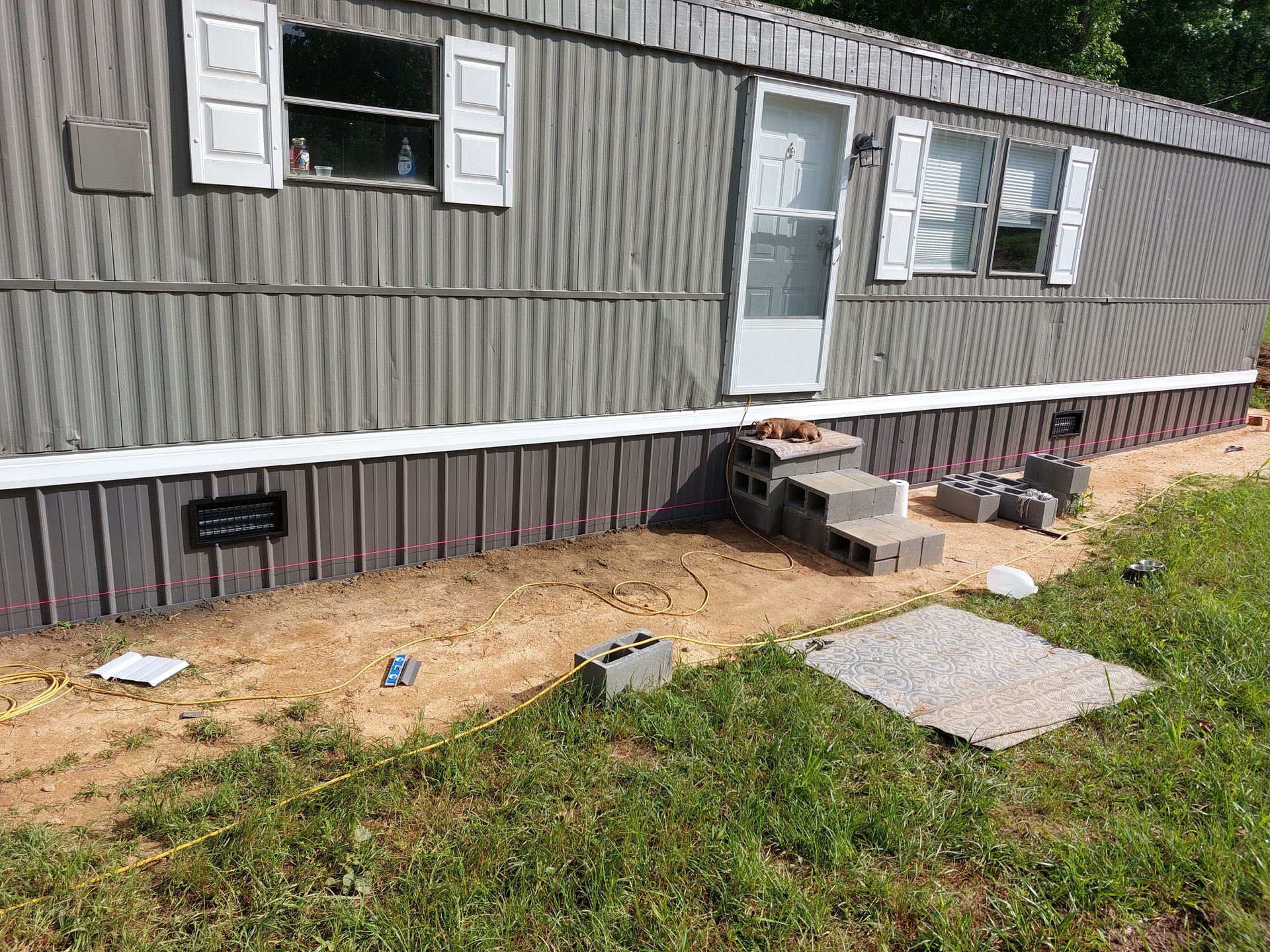 Gray mobile home exterior with small concrete steps, dirt yard, and green grass patch