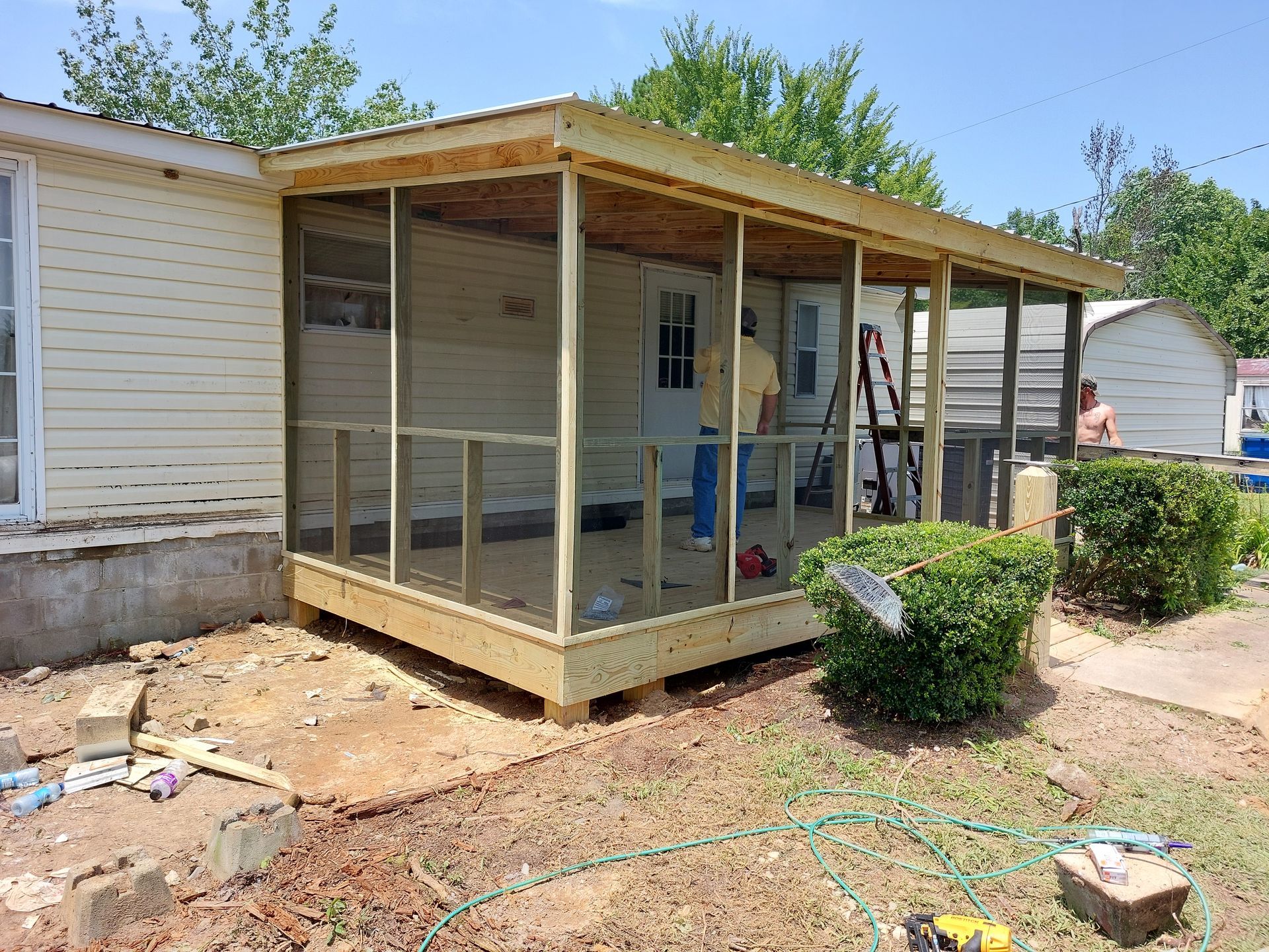 Screened porch under construction beside a white house, with wooden framing and unfinished ground.