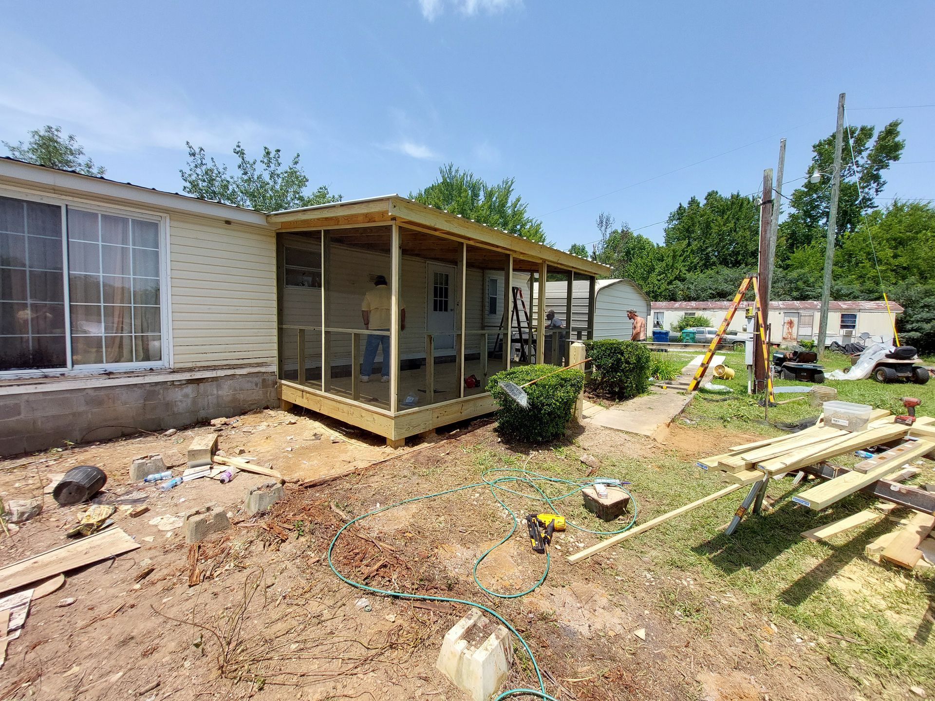 House exterior with a porch under construction, dirt yard, and lumber stacked nearby