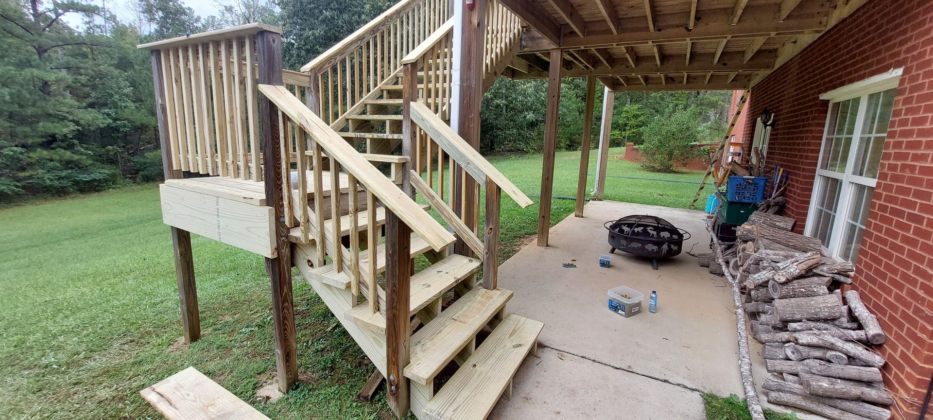 Wooden backyard stairs and landing beside a brick house, with a fire pit on a concrete patio.