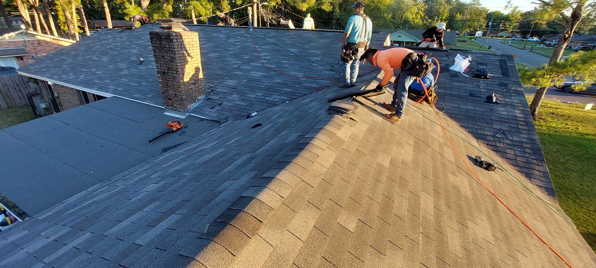 Workers repairing a sloped roof with dark shingles at a residential home in daylight