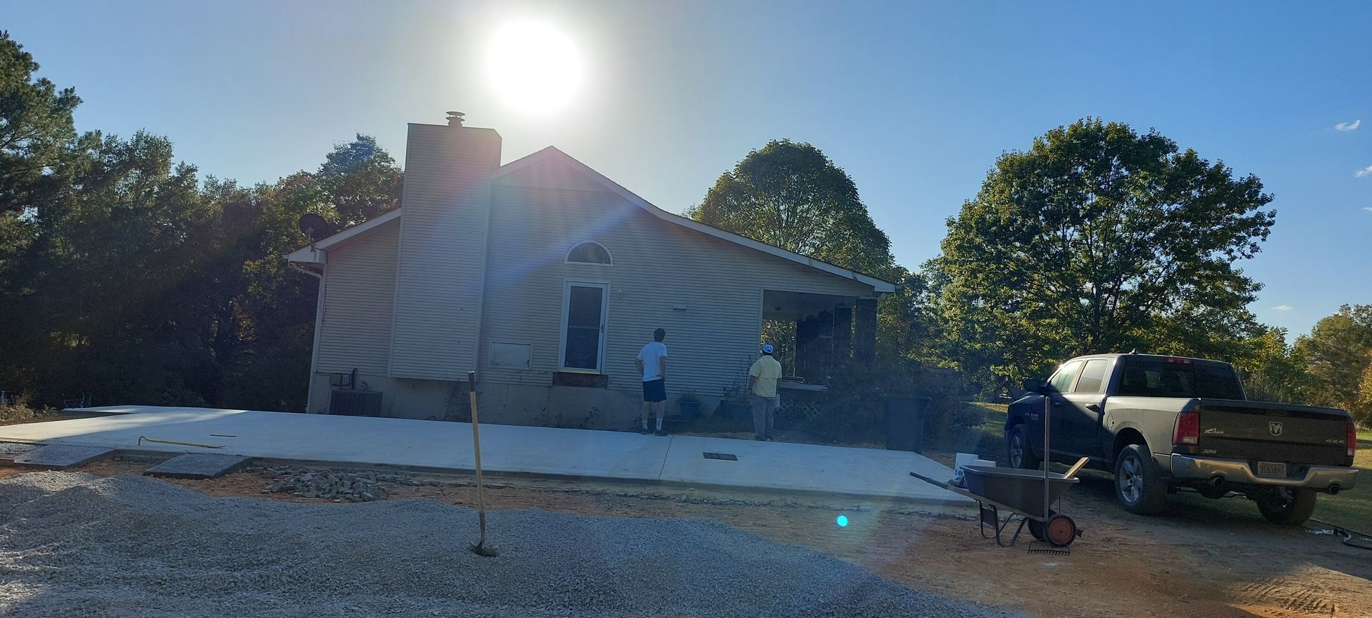 Sunlit damaged house with roof tarp, gravel yard, and pickup truck in front yard
