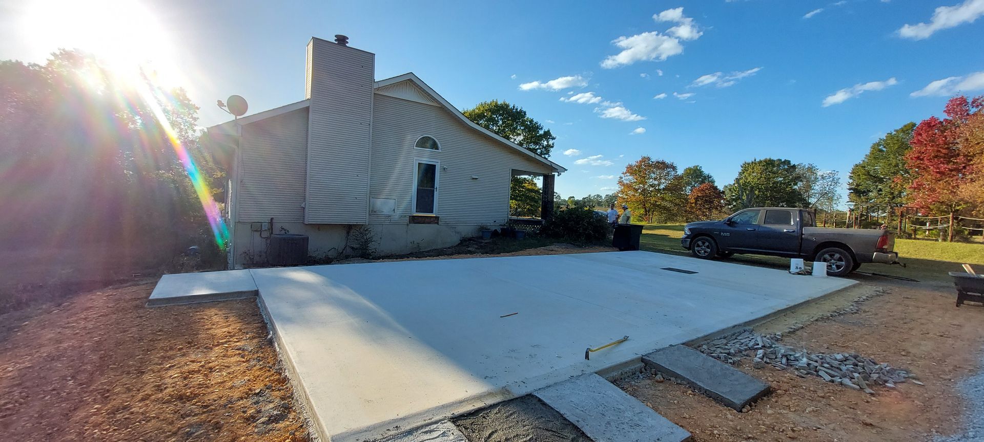 White house with a wide concrete driveway, parked pickup truck, and sunny yard with autumn trees
