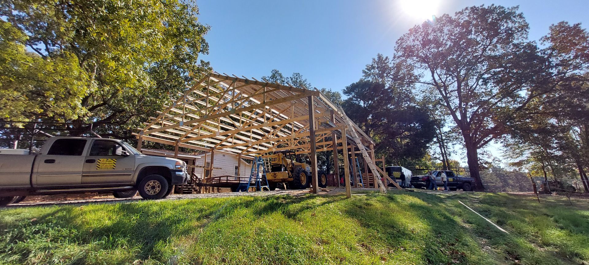 Truck beside a wooden pavilion under construction in a sunny park with trees and grass