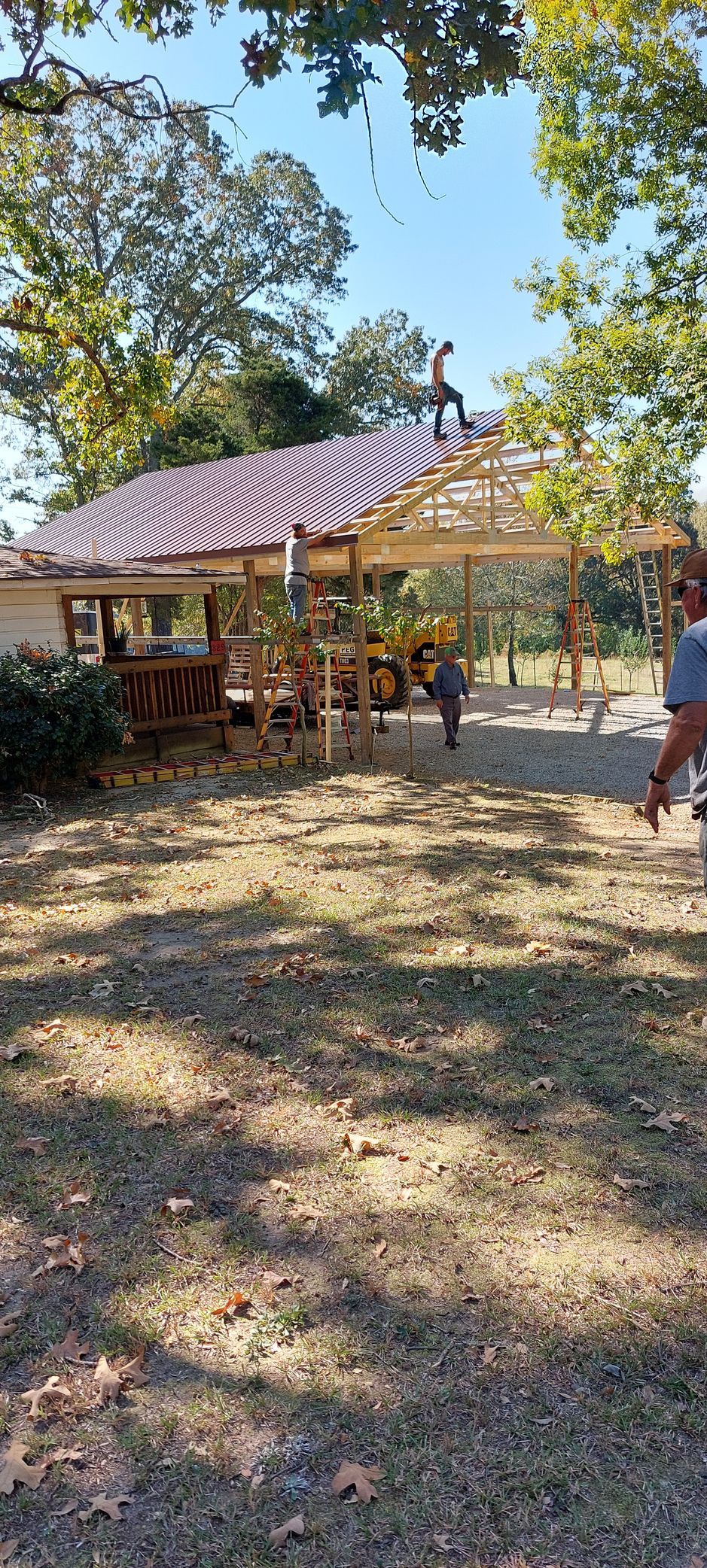 Outdoor pavilion with a striped canopy and people standing in a dry, grassy park under trees.