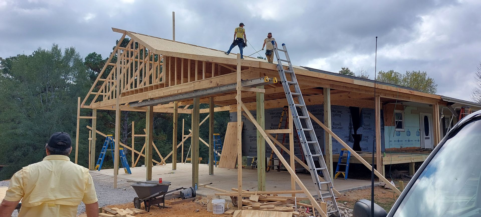 Workers building a wooden house frame with ladders and scaffolding on a construction site