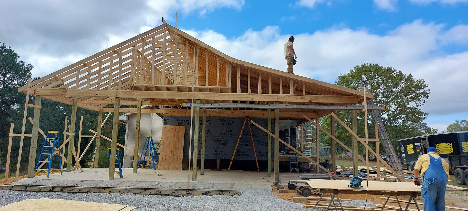 Framed house under construction with roof trusses, scaffolding, and workers on site