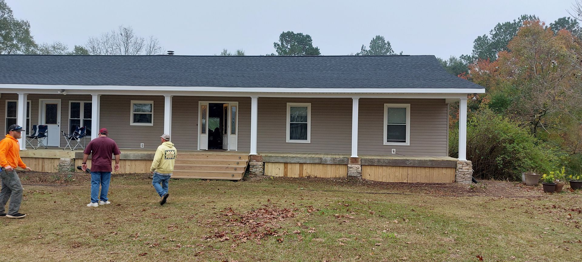 Three people walking across a leaf-covered yard toward a single-story house with a front porch
