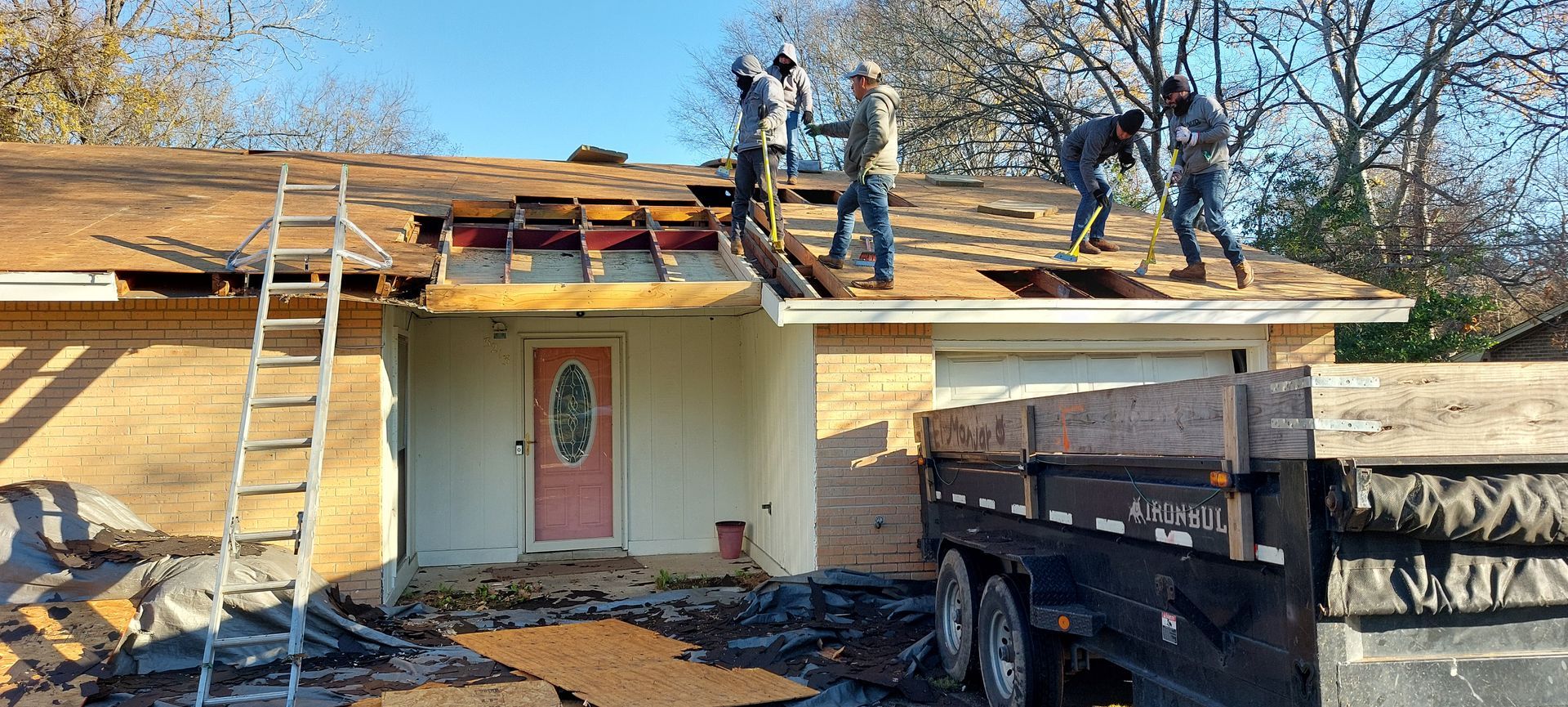 Workers repairing a roof with ladders and tools on a house in daylight