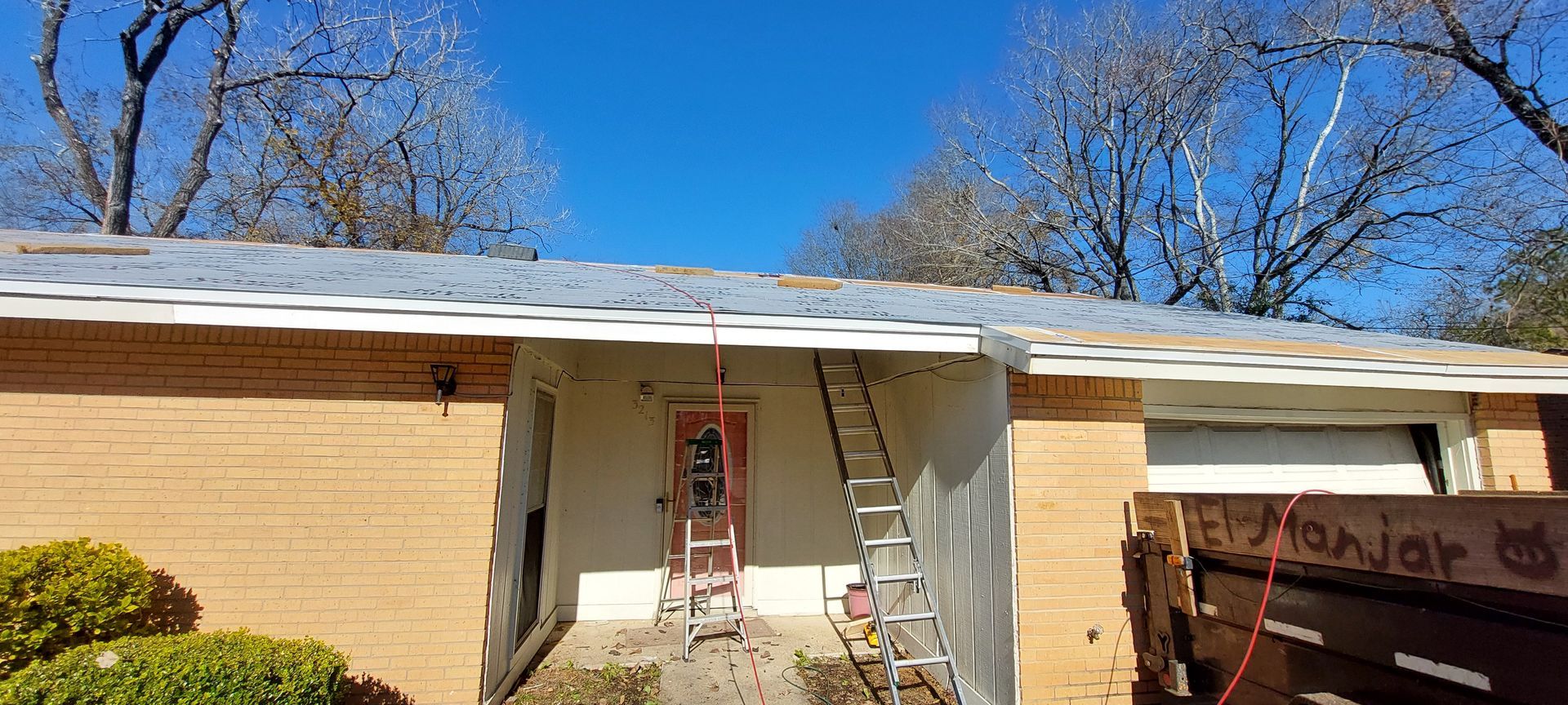 Front view of a beige house with a ladder by the front door and a carport on the right