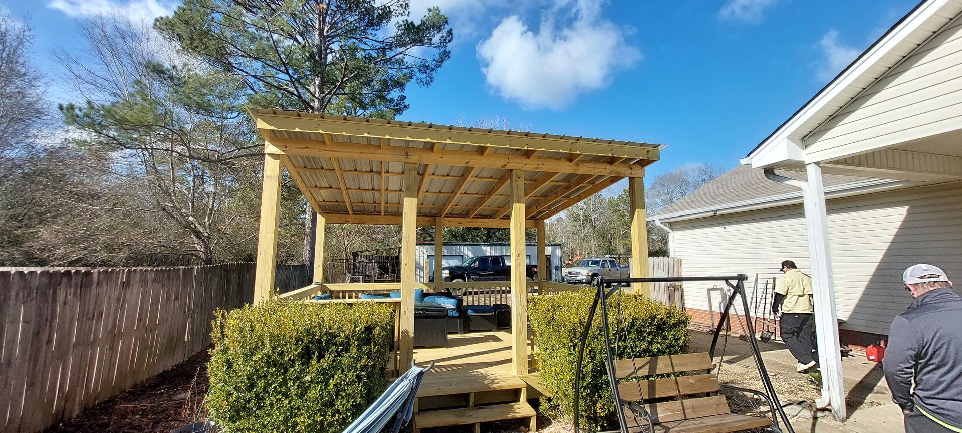 Wooden backyard deck and pergola under construction beside a house, with tools and workers nearby