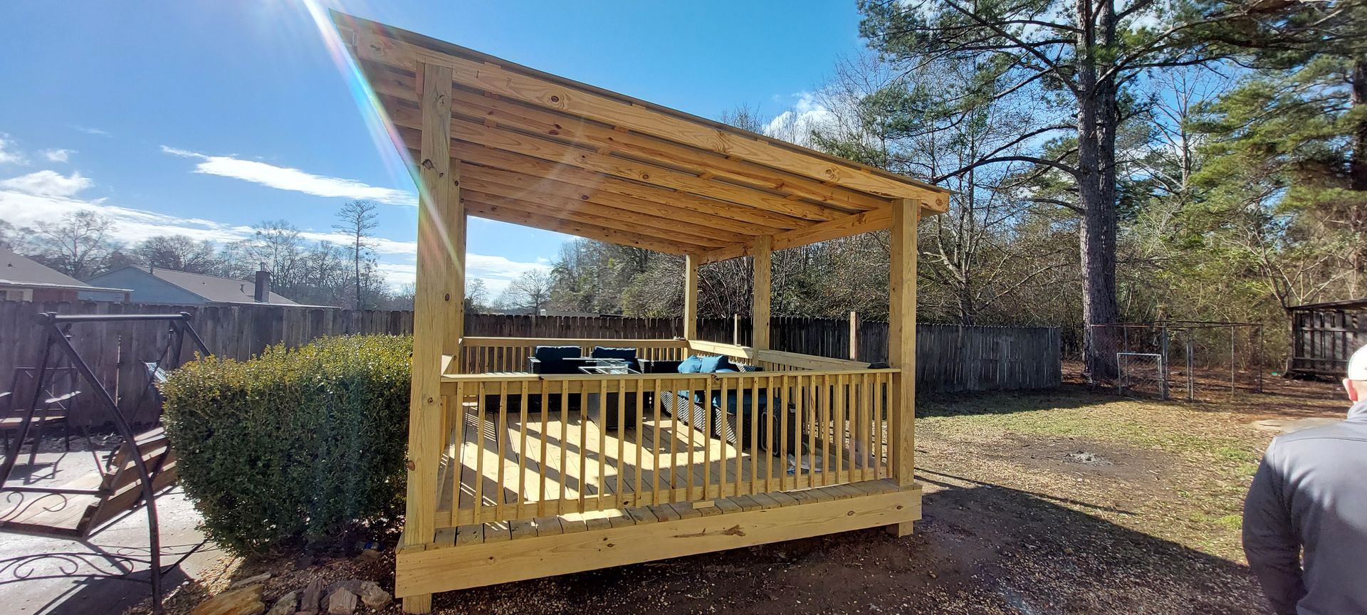 Yellow wooden gazebo on a sunlit outdoor deck with mountains and trees in the background