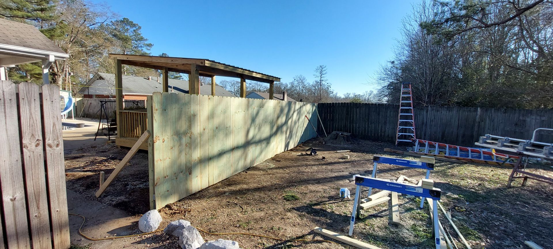 Backyard with a small shed, green fence panels, and outdoor furniture under clear blue sky