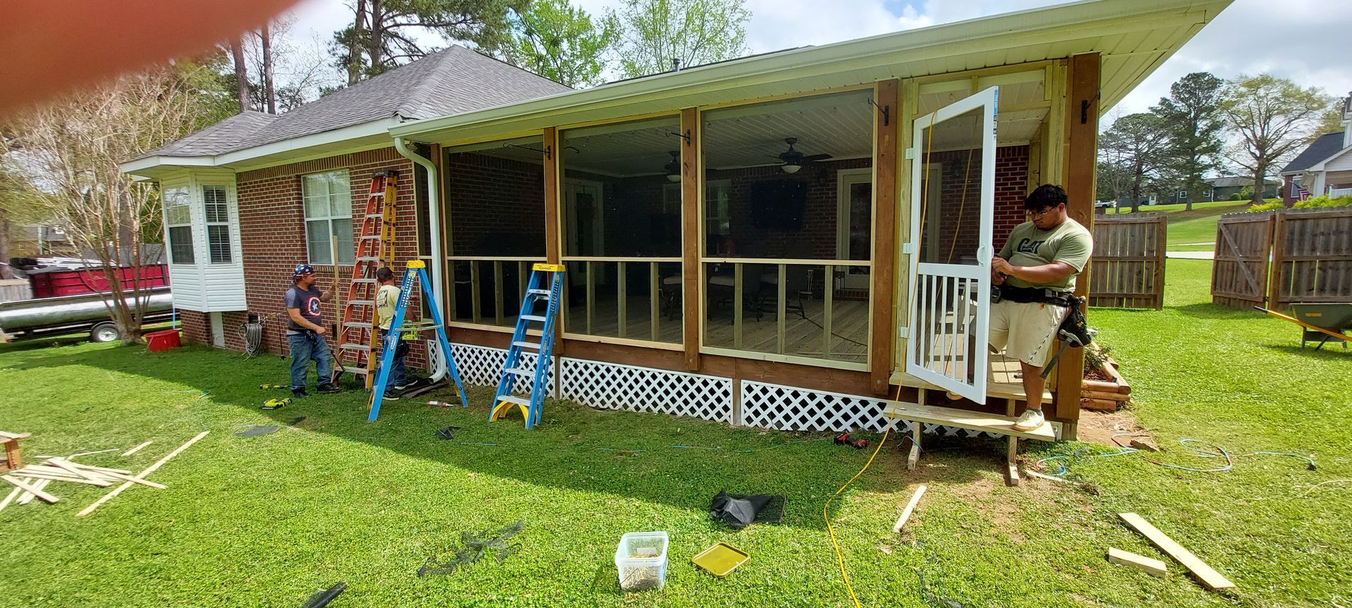 People working on a covered porch and deck with blue railings on a sunny lawn