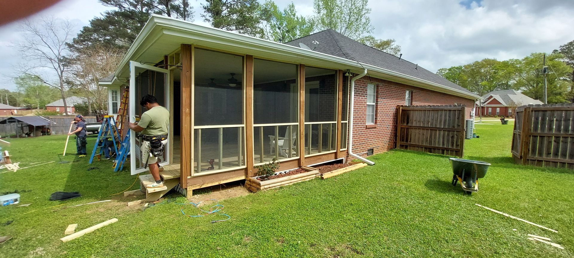 Screened backyard porch addition on a house, with a person working near the left side and a fenced lawn.