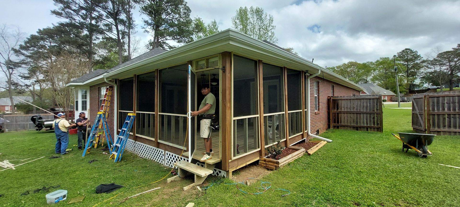 People working on a screened porch addition beside a house in a grassy yard