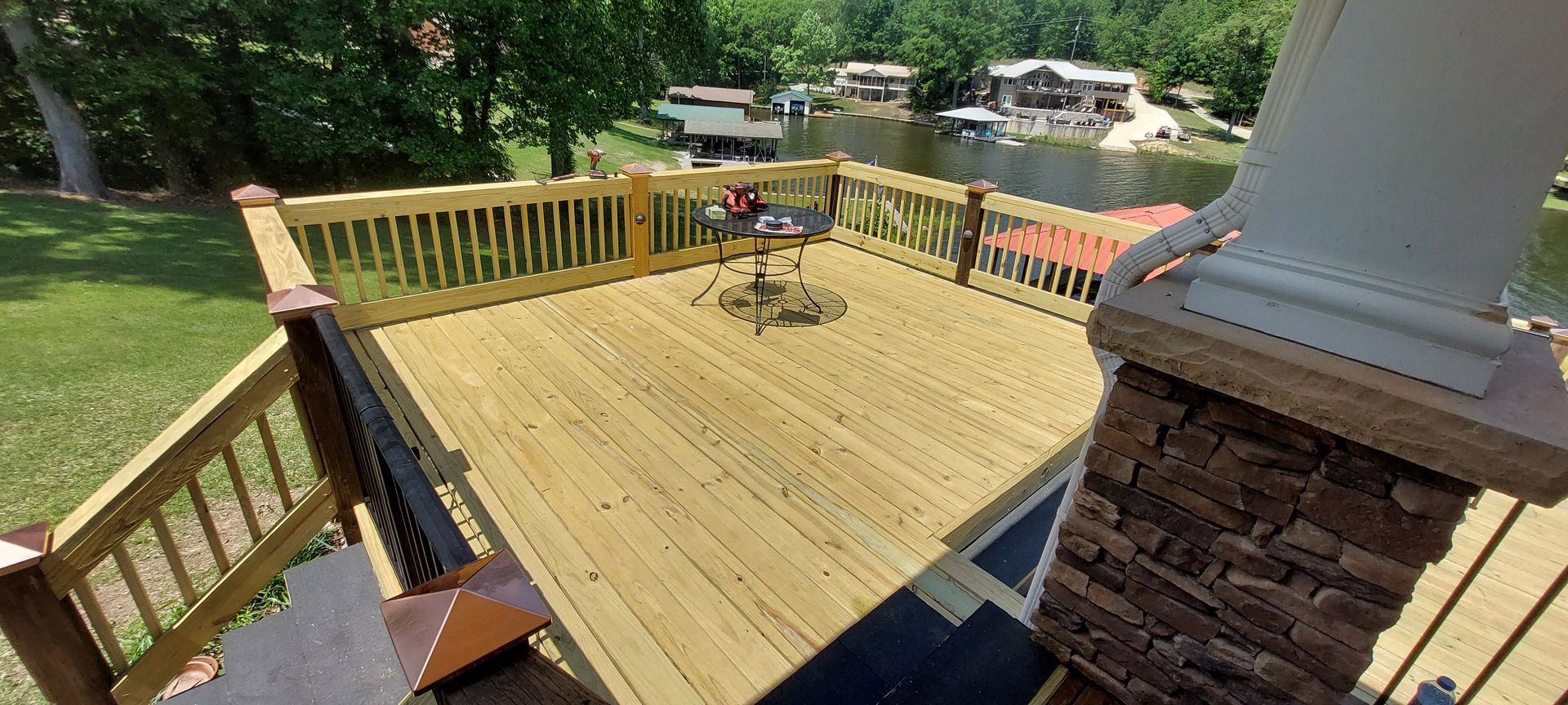 Wooden deck with railing and a brick column overlooking a green backyard and patio area