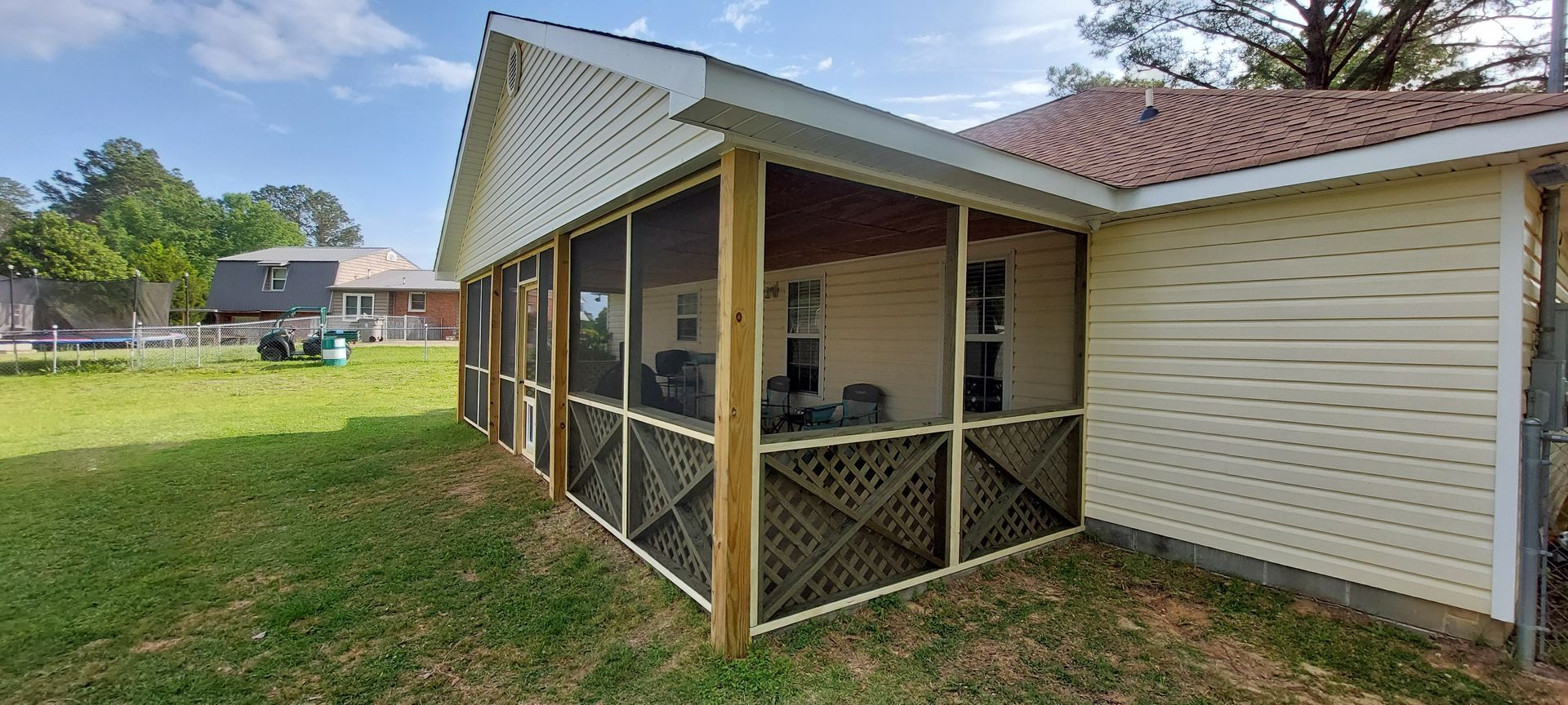 Screened back patio attached to a beige house with white trim and a red roof, overlooking a grassy yard