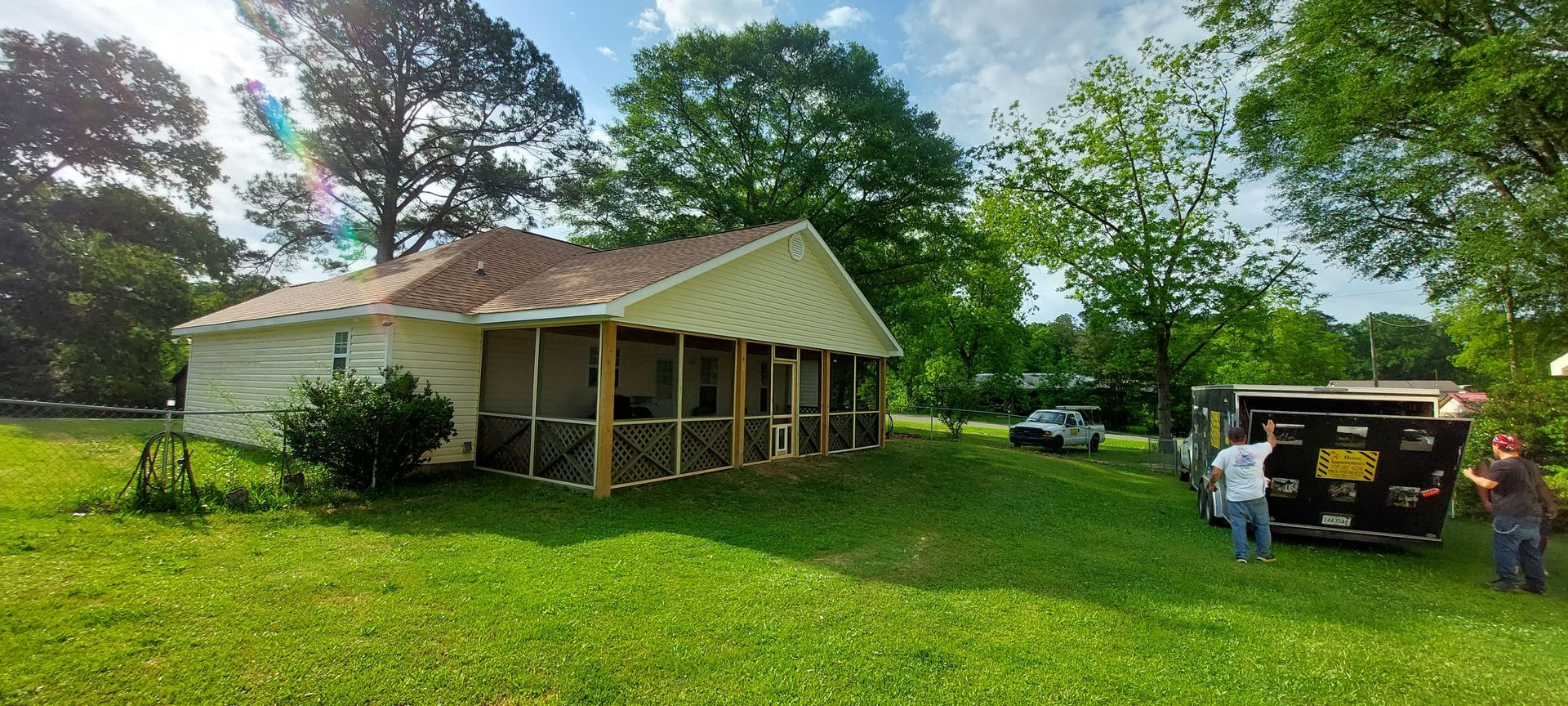 Rural house with a porch and green yard; two people stand by a black truck on the right.