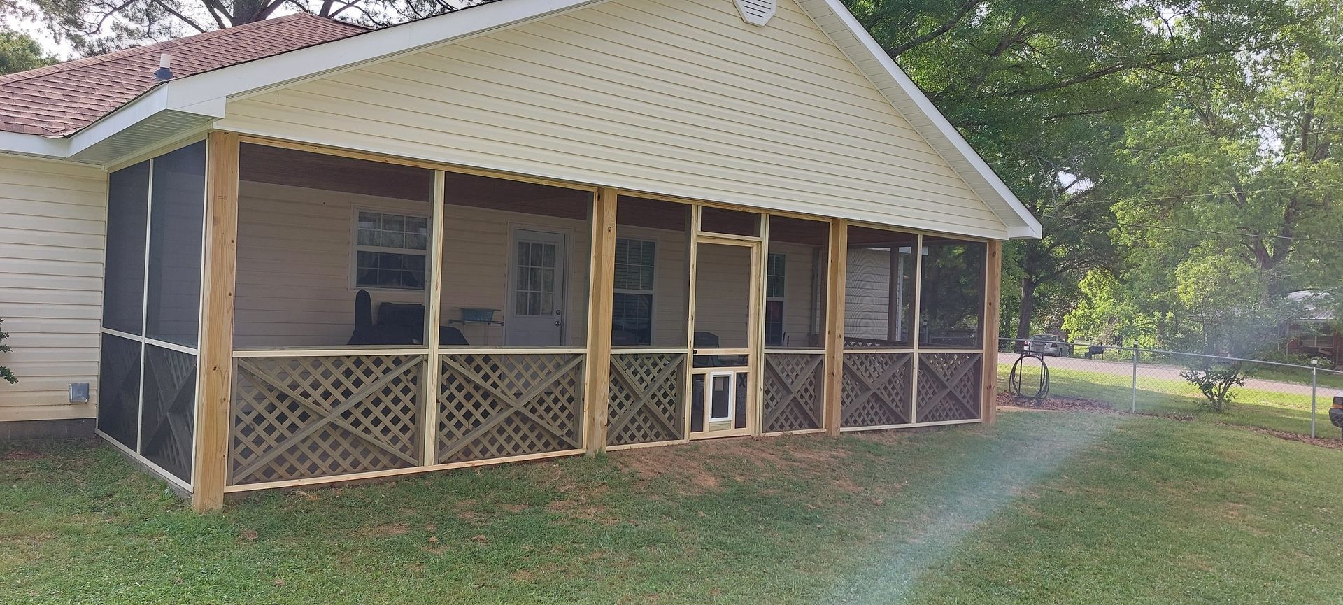 Covered porch of a cream house with screened windows and lattice railing beside a grassy yard.