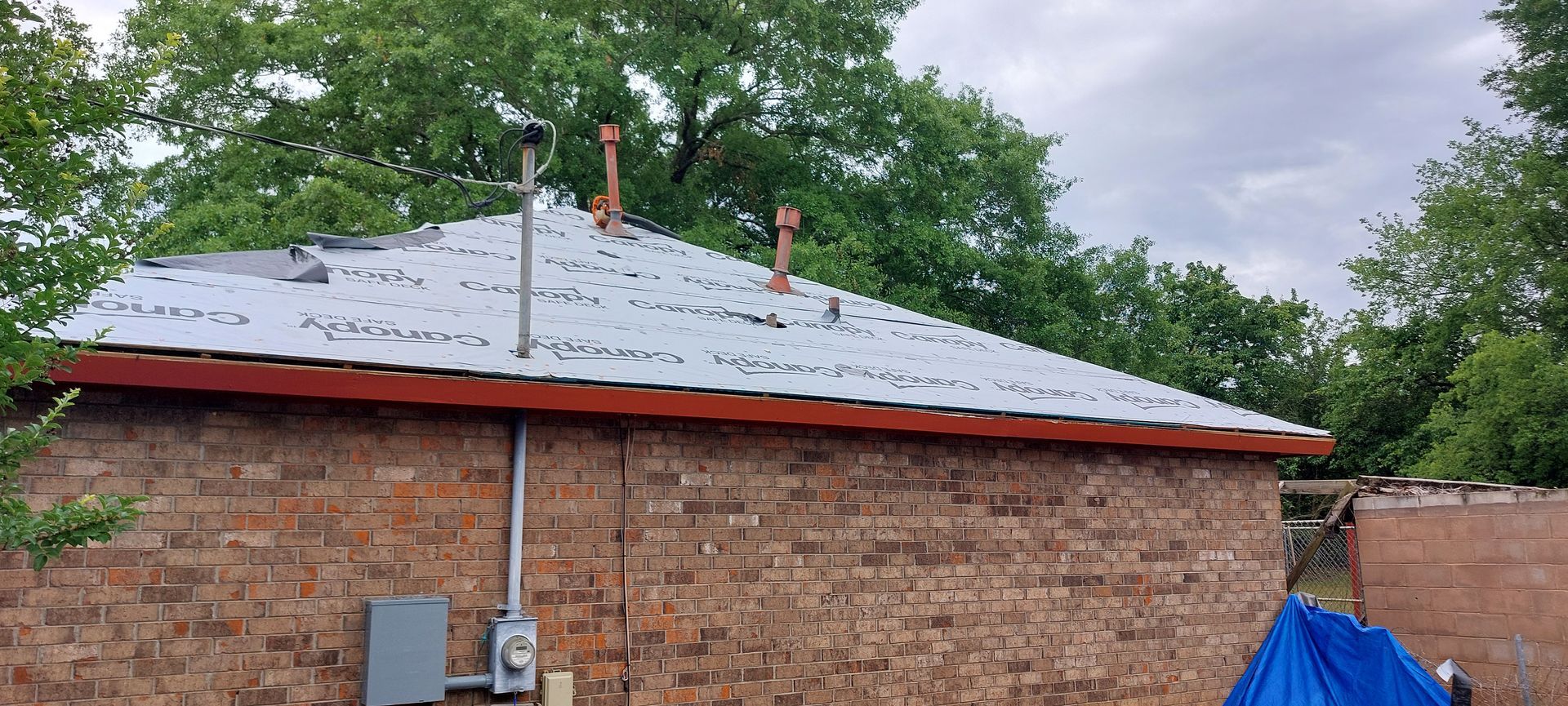 Brick house roof with gray shingles, orange trim, and two vent pipes under cloudy sky