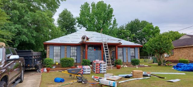 Single-story brick house with workers renovating the front yard, ladders, tools, and scattered materials.