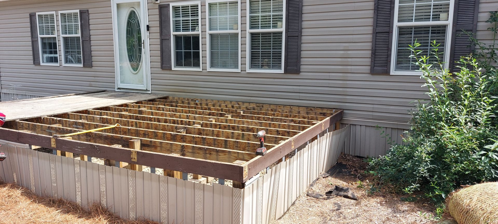 Raised garden bed with a wooden frame in front of a house, filled with soil and grid supports