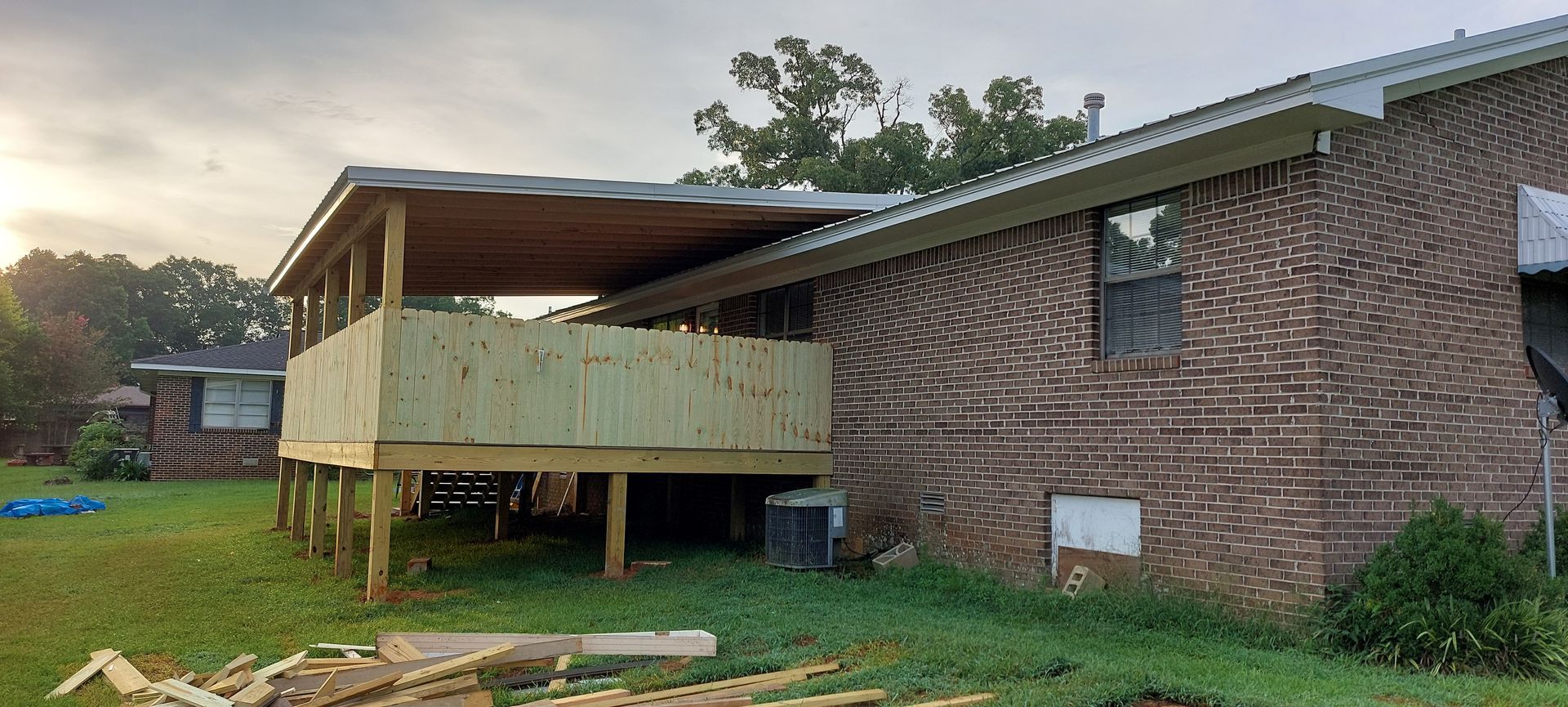 Wooden house under construction with a covered porch and green yard at sunset