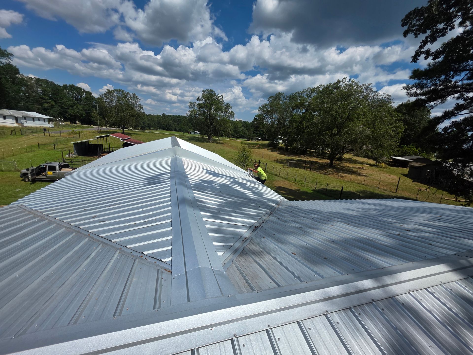 Silver metal roof with a central ridge, viewed over a green landscape under a cloudy sky
