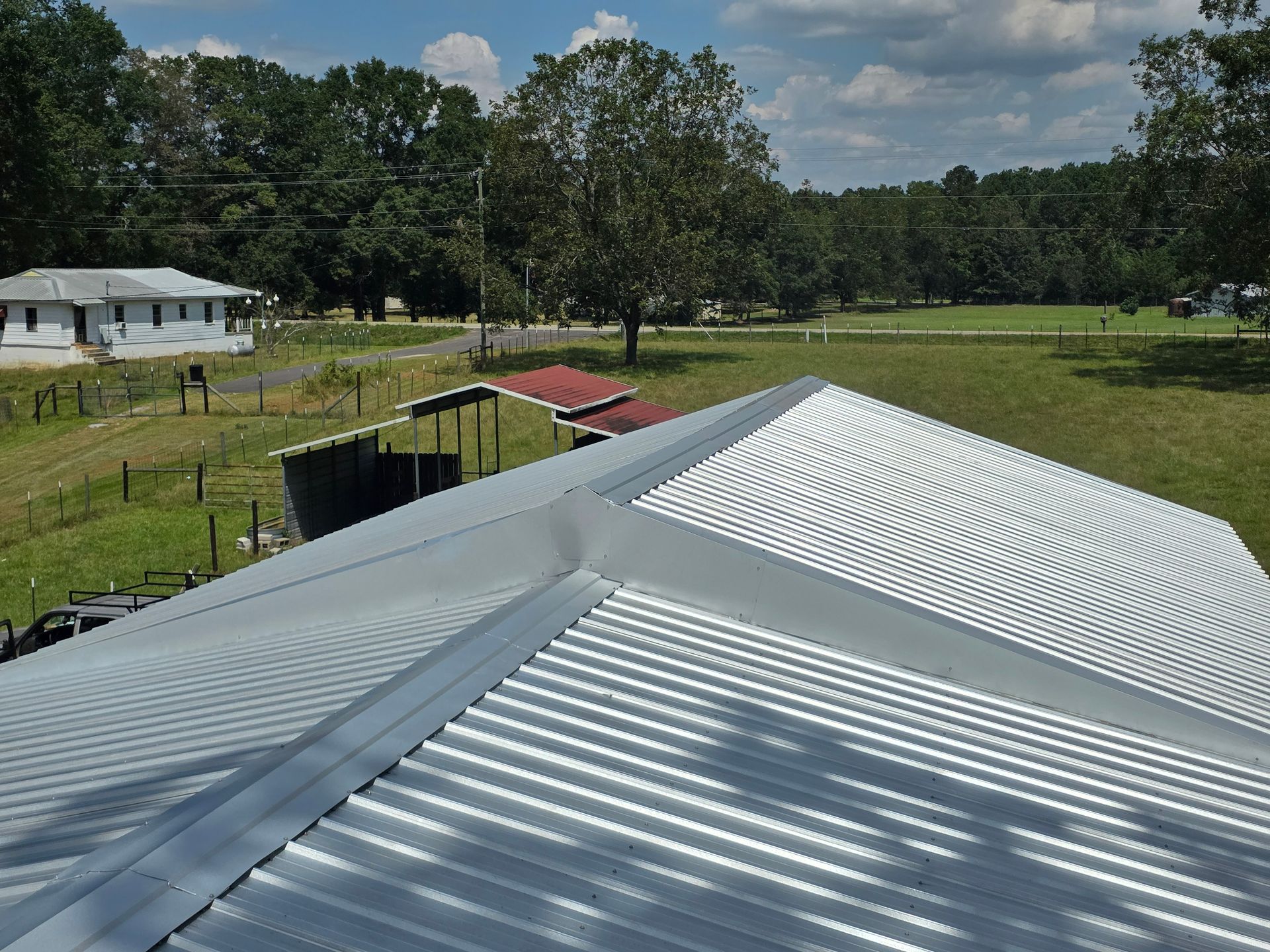 White corrugated metal roof overlooking a grassy yard, trees, and a small barn under a cloudy sky