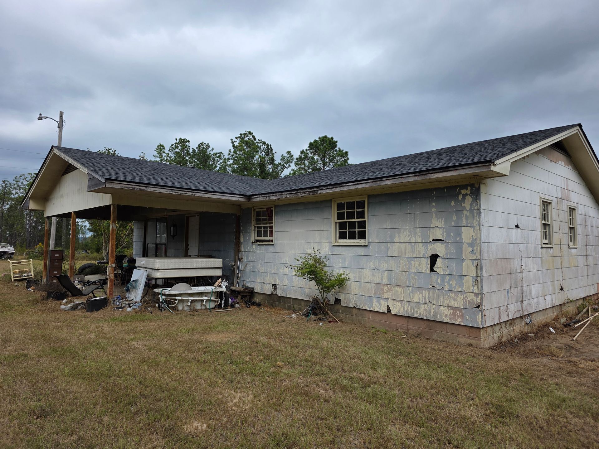 Single-story house with damaged exterior siding and a covered front porch on a grassy lot.