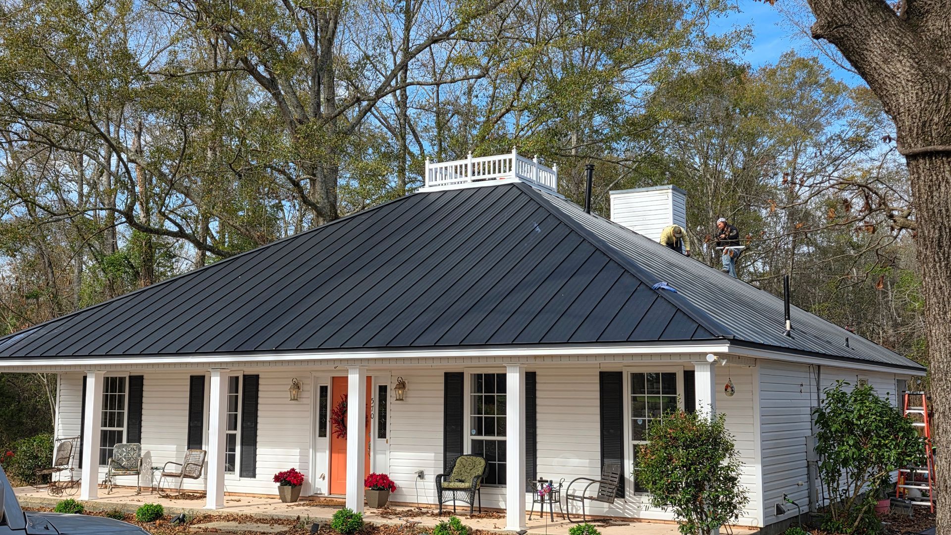 Single-story white house with a dark roof, front porch, and trees in the yard.
