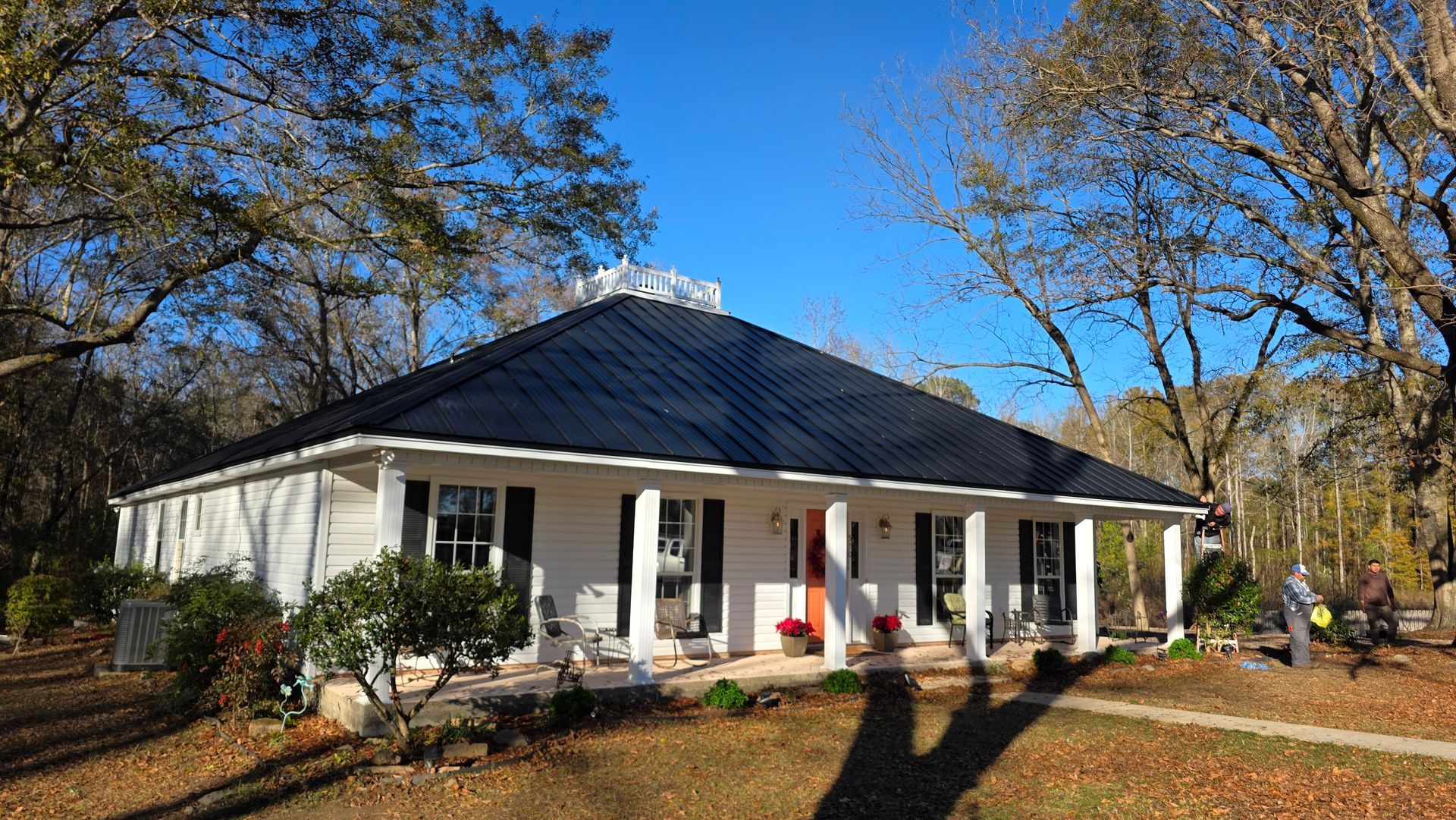 White house with dark roof, front porch, and autumn trees in a sunny yard