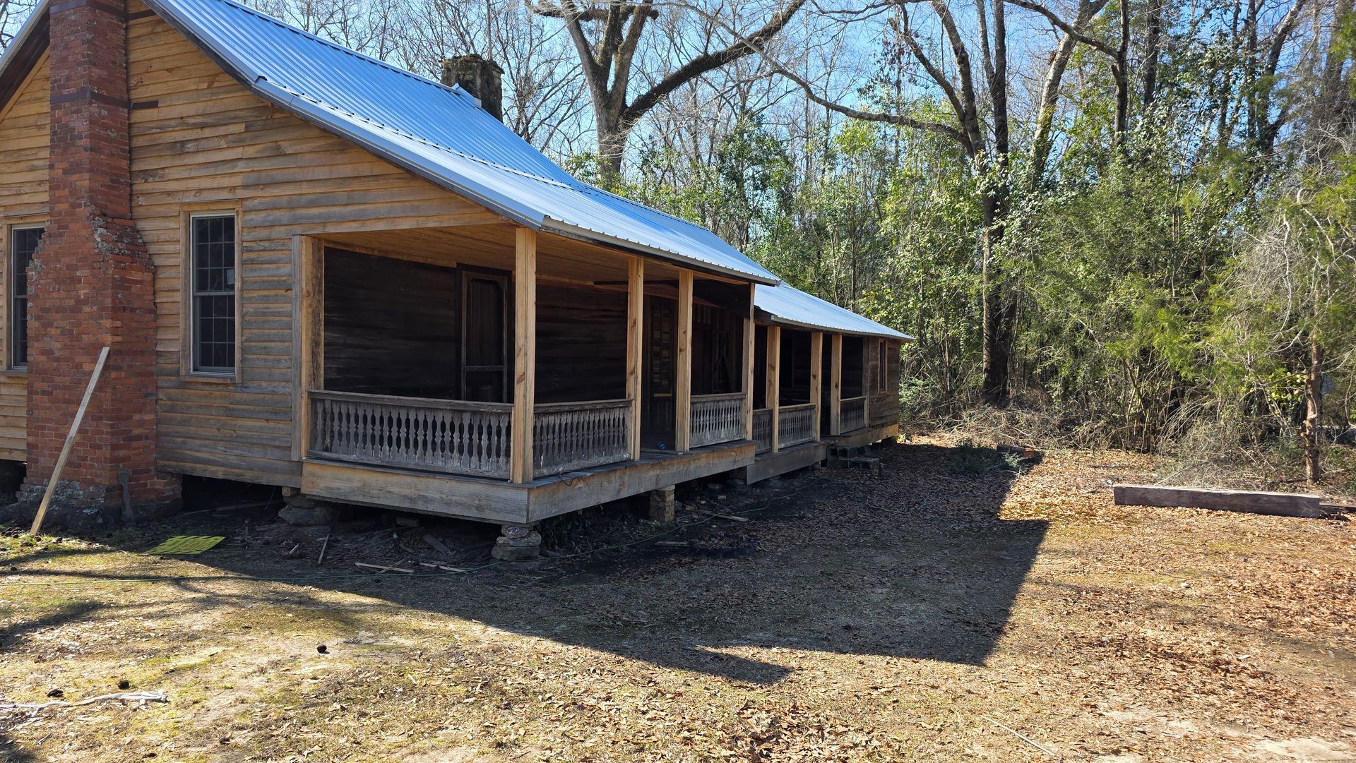 Rustic wooden cabin with blue metal roof and front porch in a wooded clearing