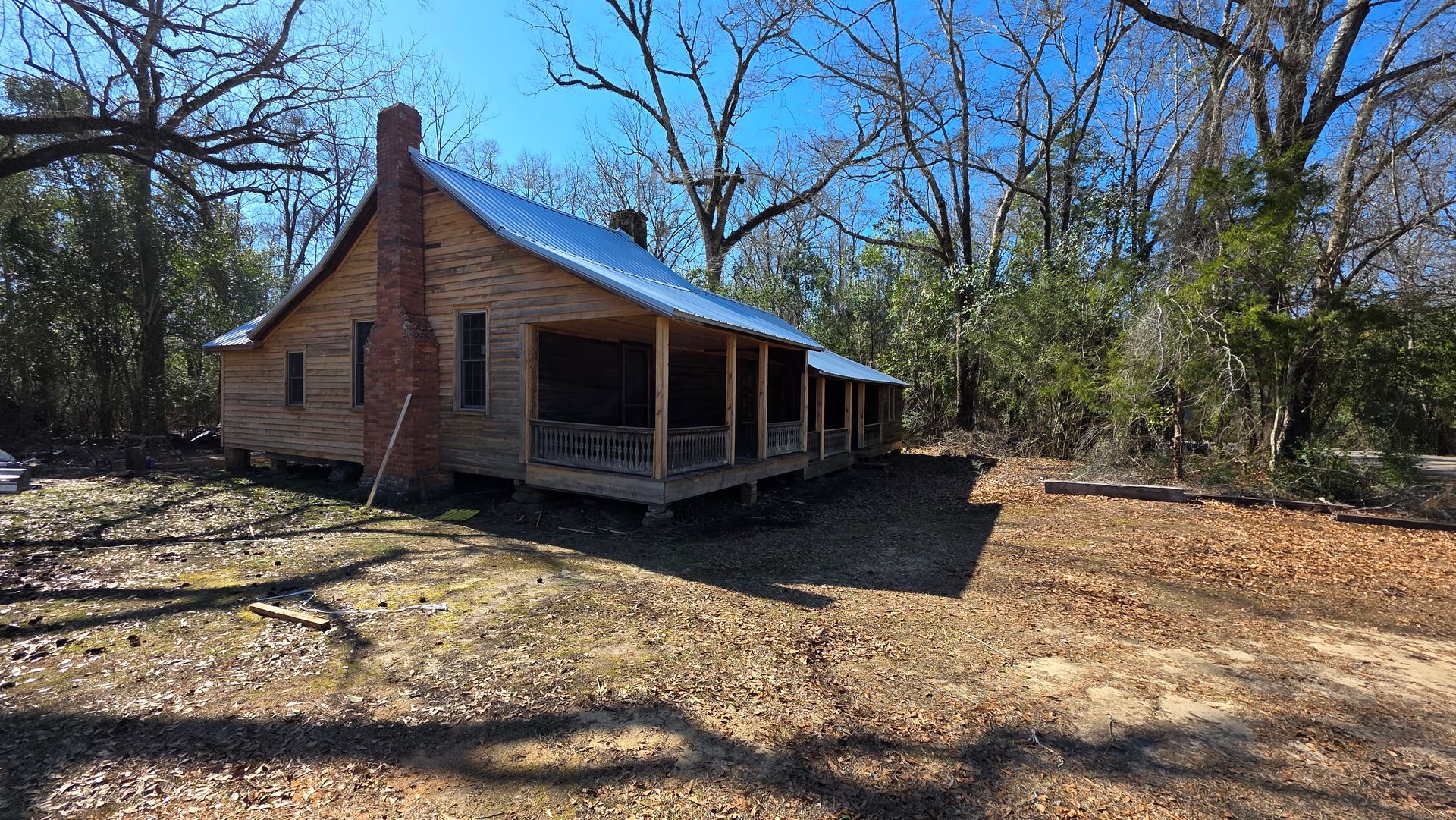 Small rustic brick cabin with a blue metal roof and covered porch in a wooded clearing
