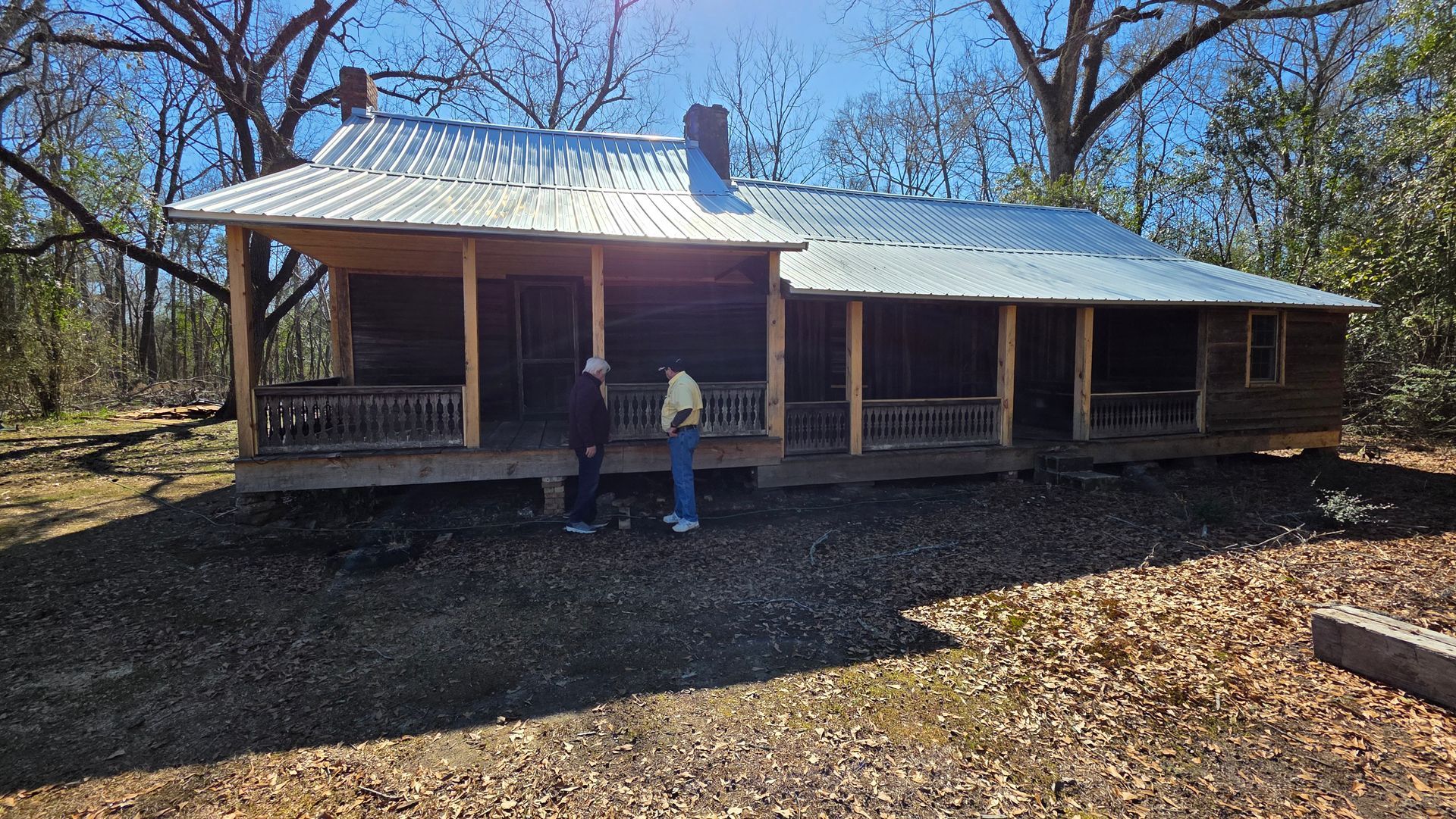 Porch-front cabin in a wooded clearing with two people standing outside in sunlight