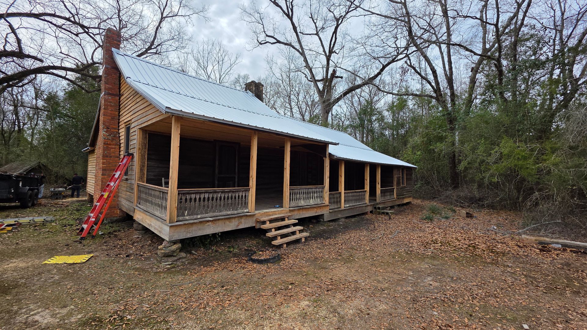Rustic cabin with a front porch and metal roof in a wooded clearing on a cloudy day